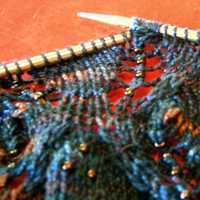 closeup of blue variegated lace knitting with beads and nupp on needles